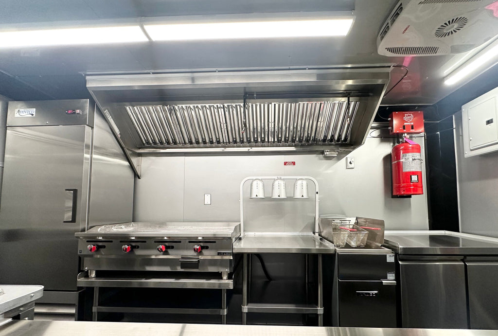 Interior cook line of the 14 FT Burger Trailer with the 48 inch griddle, heat lamp and stainless vent hood