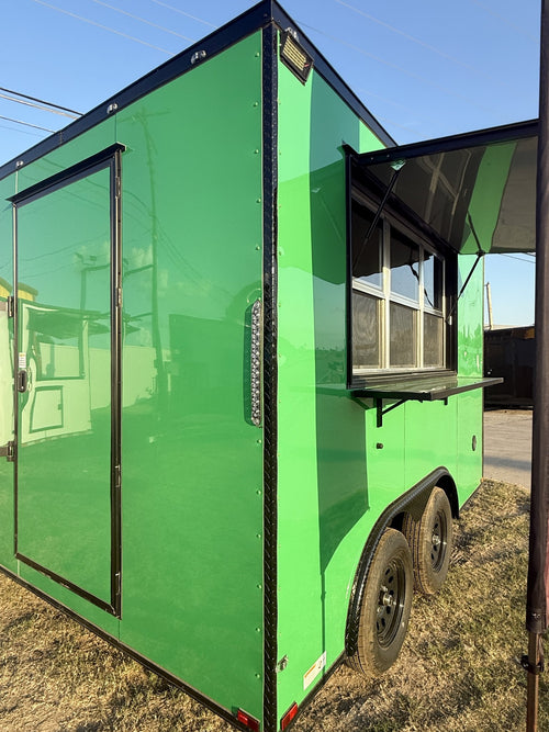 A bright green food truck trailer parked outdoors on dry grass under a blue sky, with a side door and an open serving window visible.