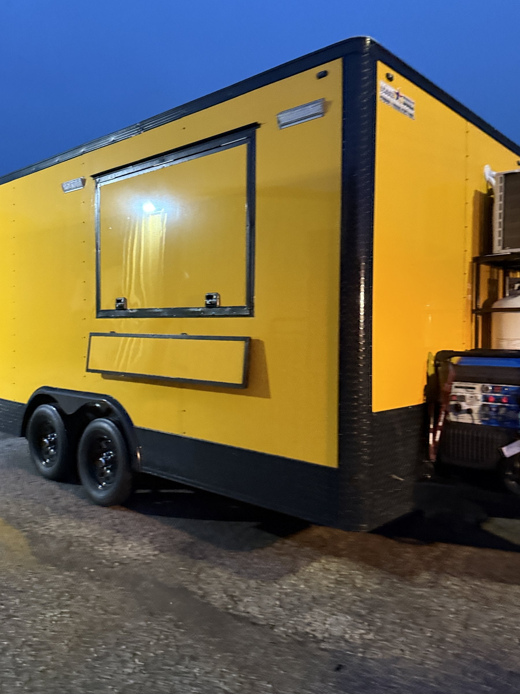 14 FT yellow cooking trailer, exterior front three-quarter at dusk with the serving window lit