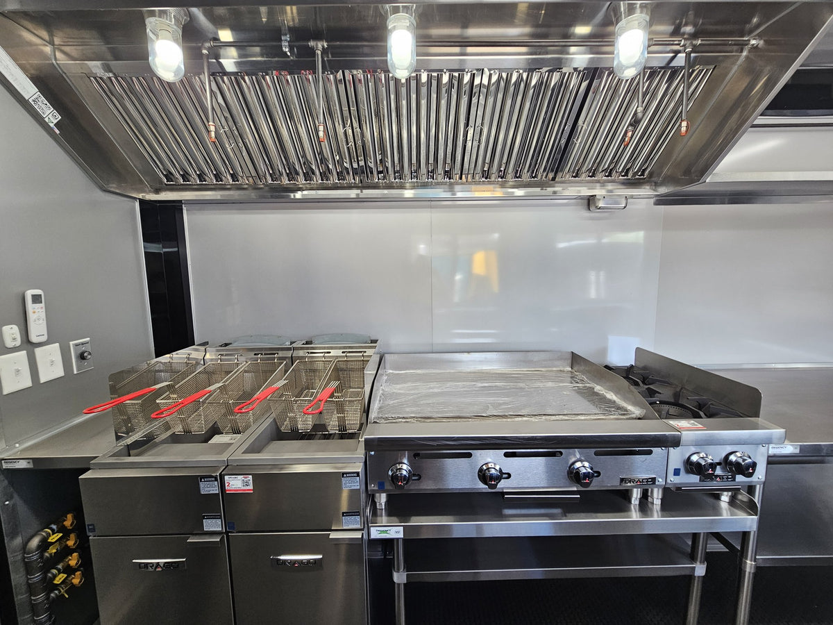 Commercial kitchen equipment including a stainless steel deep fryer with baskets, a flat top griddle, and a large ventilation hood with built-in lights.