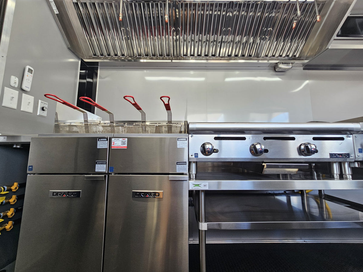 Commercial kitchen equipment including stainless steel deep fryers, a gas range, and a large overhead exhaust hood.