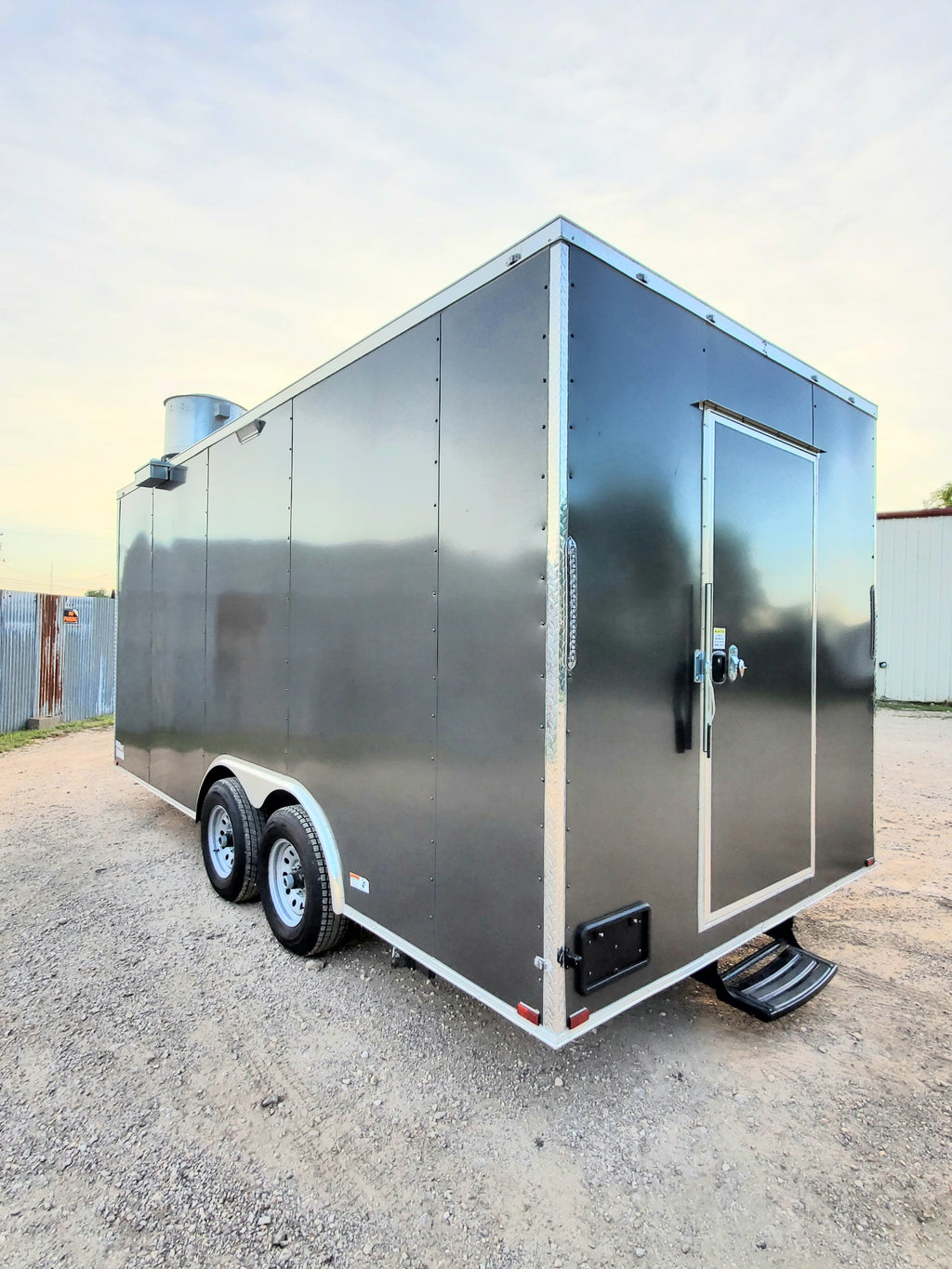 Gray enclosed trailer with a door on a gravel surface.
