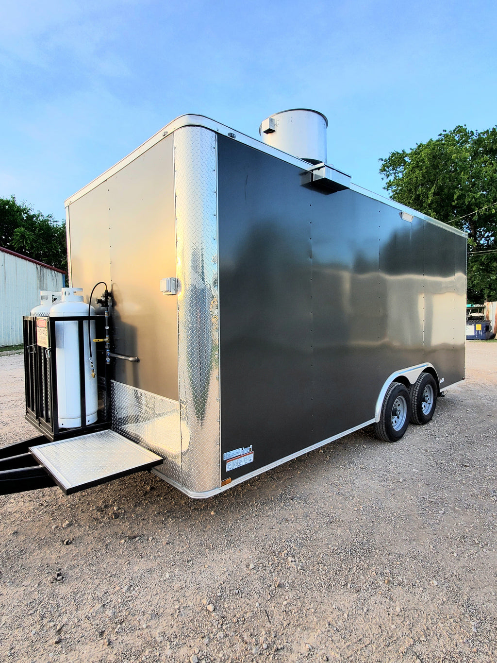Black and beige enclosed trailer on a gravel surface with trees in the background