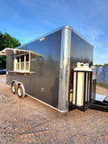 Black food trailer with a silver roof on a gravel surface under a blue sky.