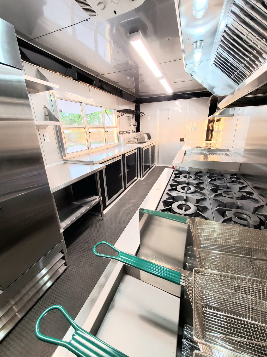 Commercial kitchen with stainless steel appliances and green handles on metal carts.