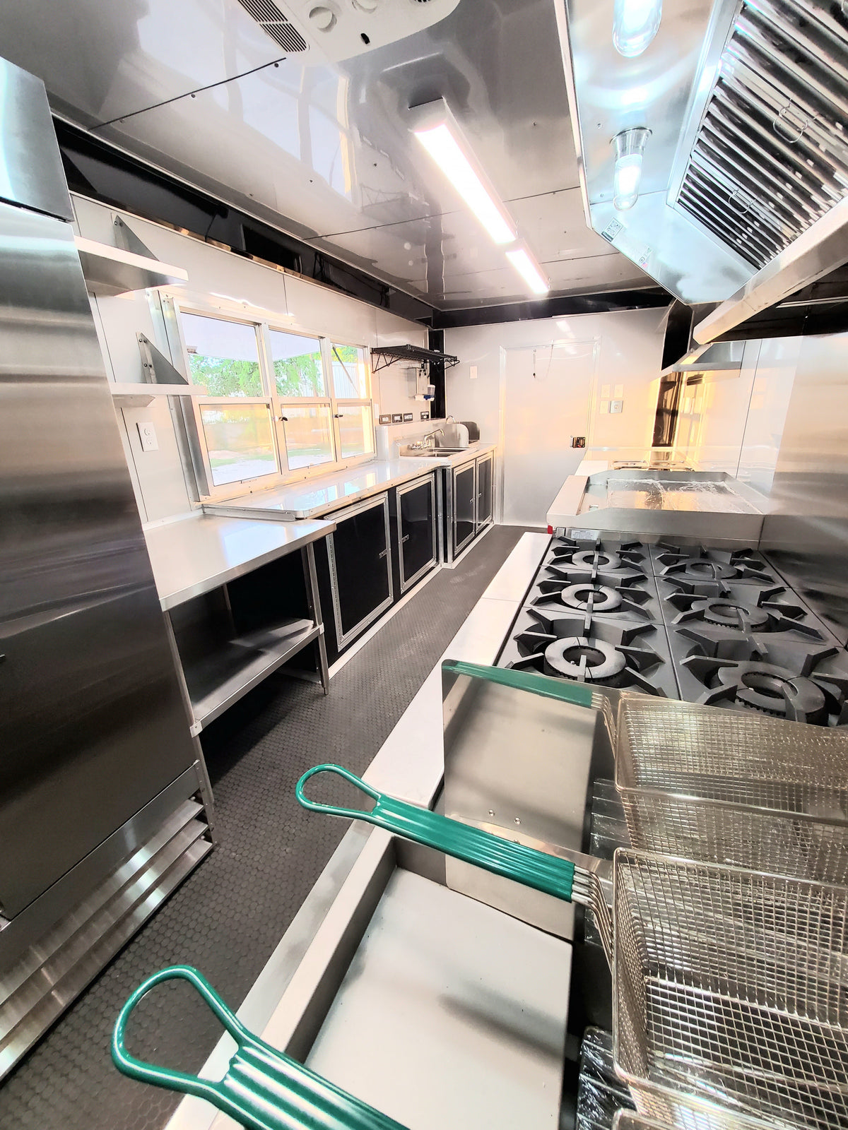 Commercial kitchen with stainless steel appliances and green handles on metal carts.