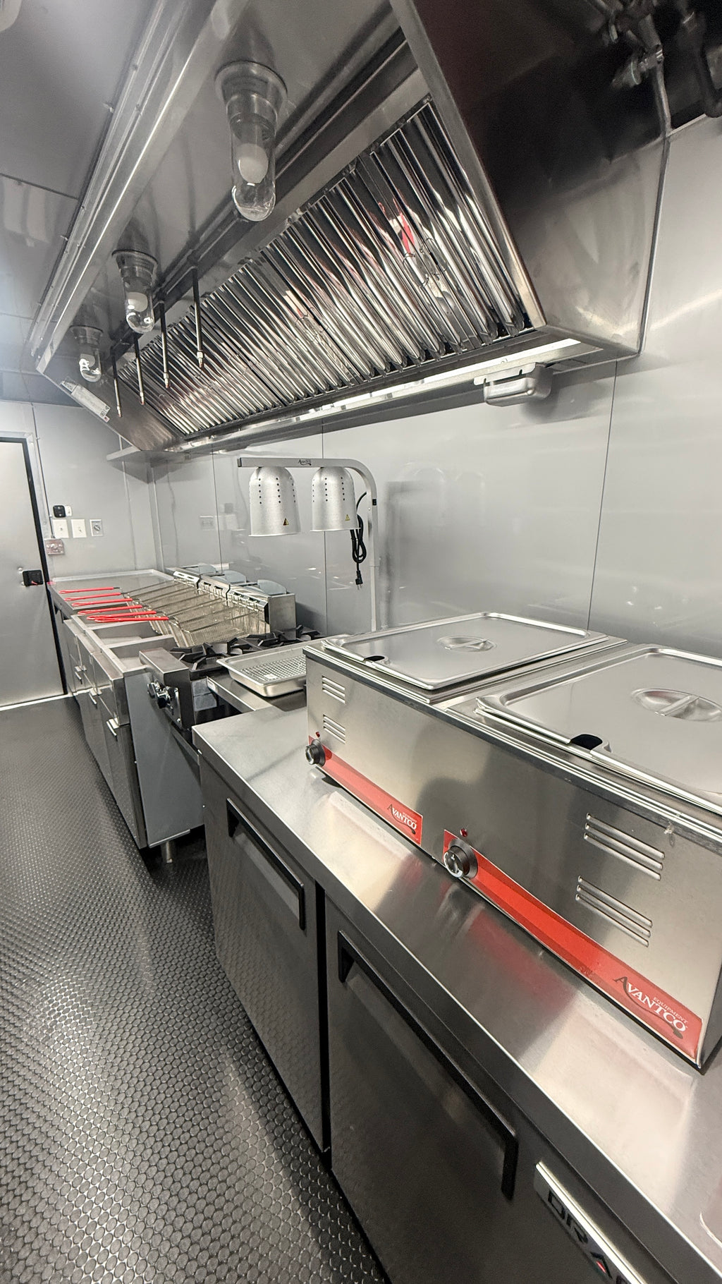 Commercial kitchen equipment including stainless steel counters, deep fryers, and a large overhead ventilation hood in a clean, industrial kitchen setting.