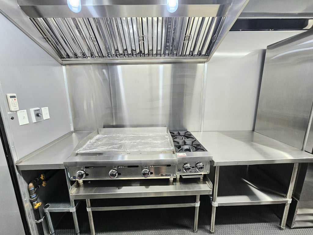 Commercial kitchen equipment including a stainless steel gas range, flat top grill, gas range hood, and work surfaces against a stainless steel wall.