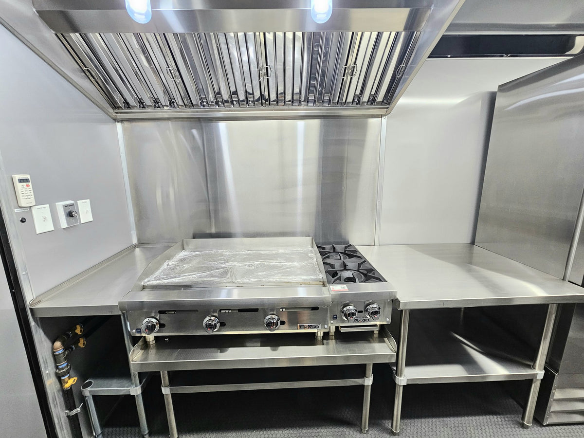 Commercial kitchen equipment including a stainless steel gas range, flat top grill, gas range hood, and work surfaces against a stainless steel wall.