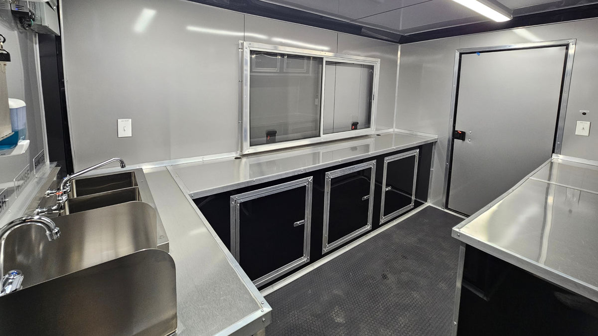 Stainless steel prep area inside a custom concession trailer, with a double sink, sealed countertops and storage cabinets
